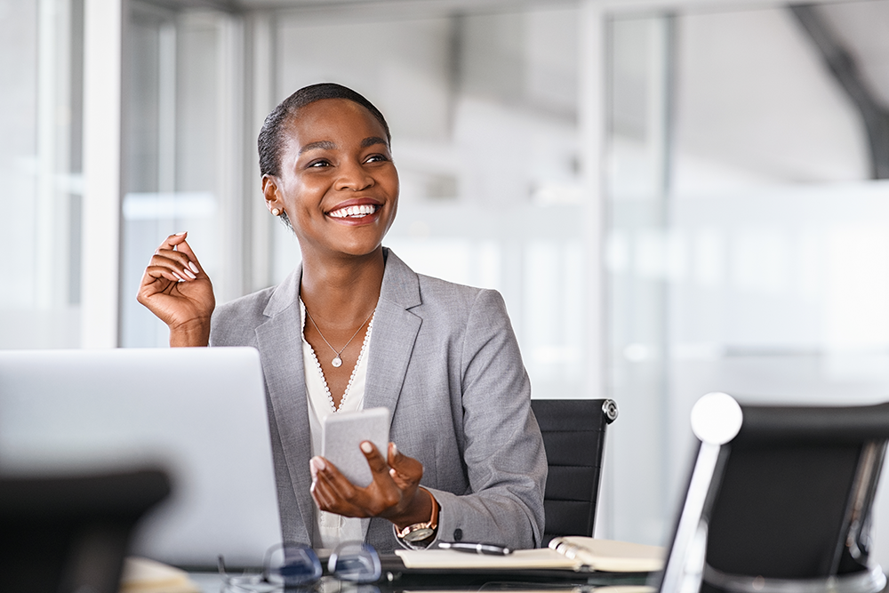 Woman sitting at a desk in front of an open laptop smiling off camera to the viewer's right